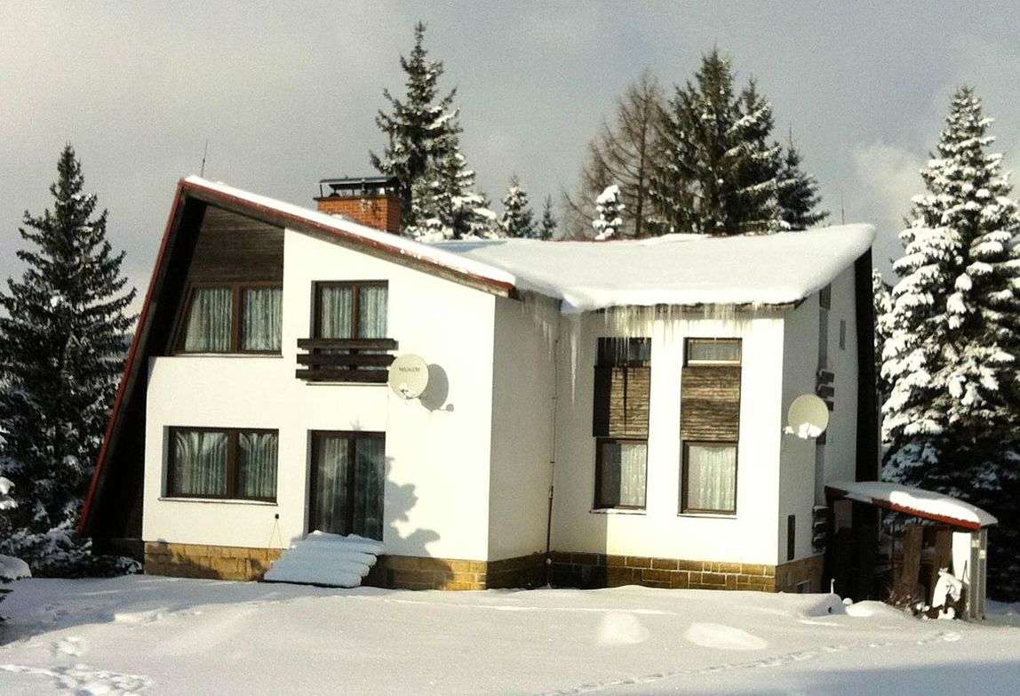 Zasněžená chata zepředu mezi smrky, starší fotka z archivu