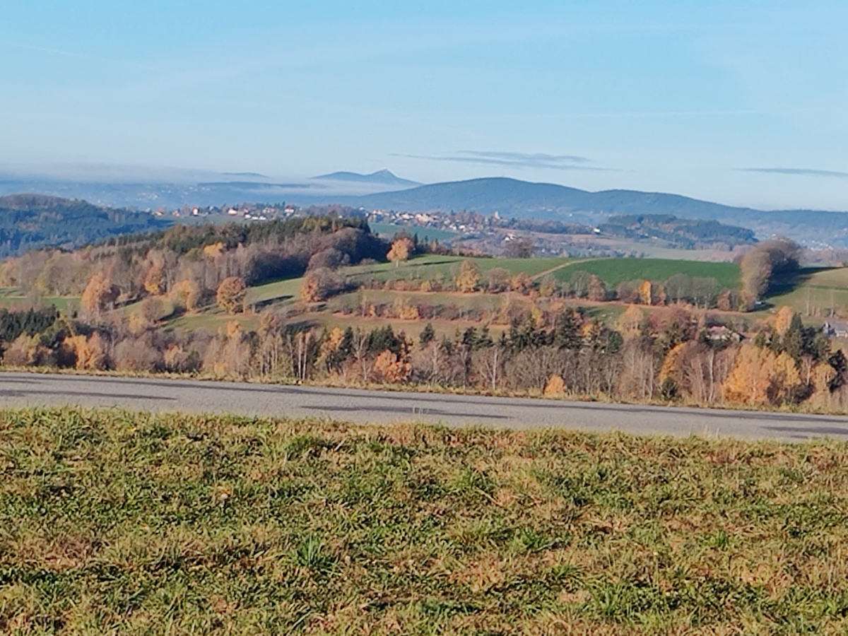 Výhled od chaty ráno: podzimní stromy, údolí s vesnicí a hřebeny