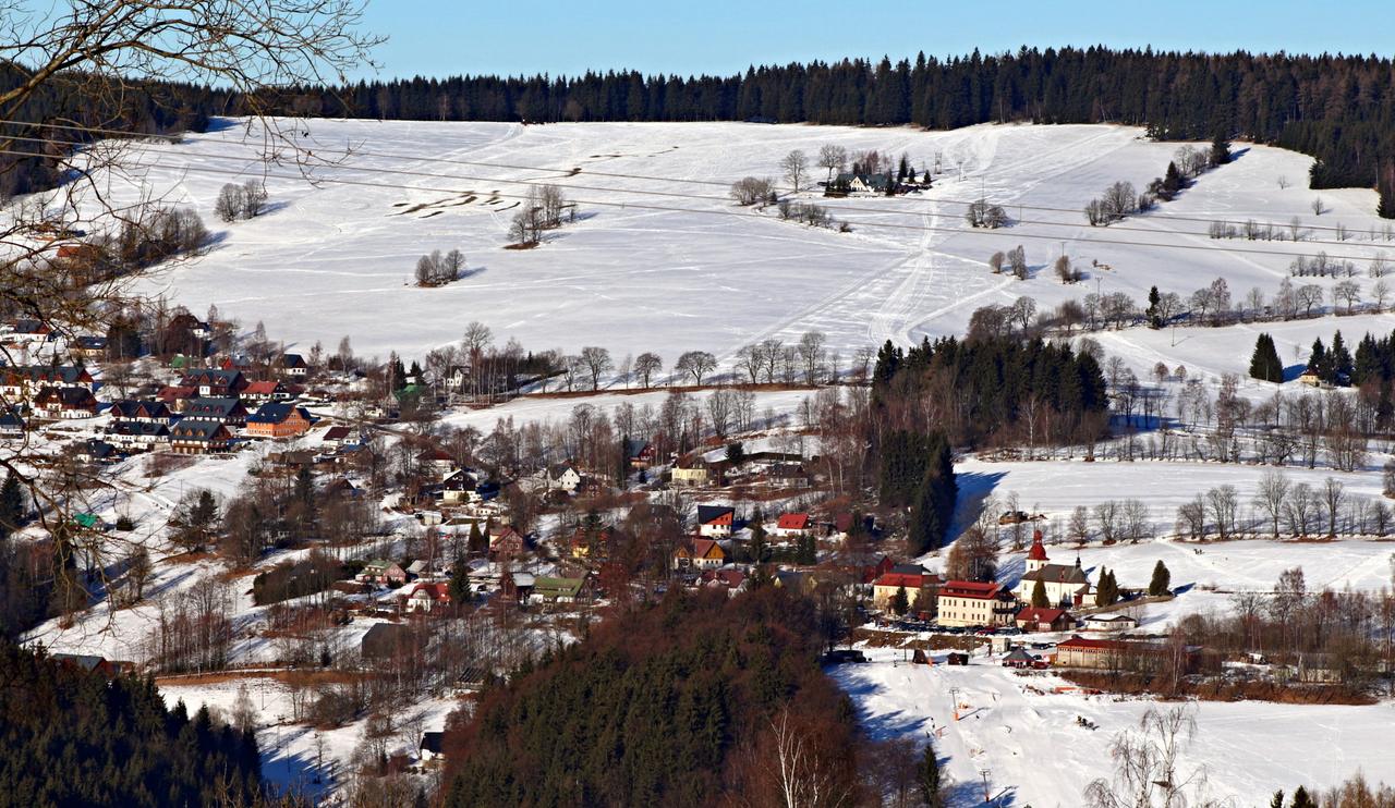 Zasněžené svahy a sjezdovky nad Vítkovicemi v Krkonoších za slunečného dne, pod nimi vesnice
